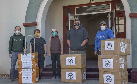 men and women standing in back of boxes of protective gear used to fight covid-19