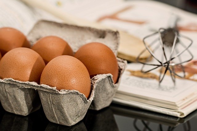 Carton of Eggs and Whisk next to a cookbook.