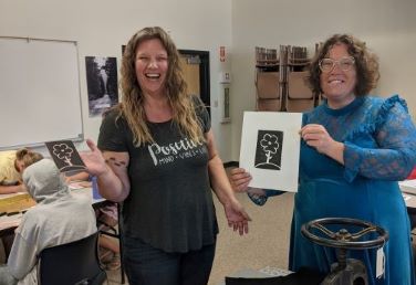 Two women hold linoleum block prints. 