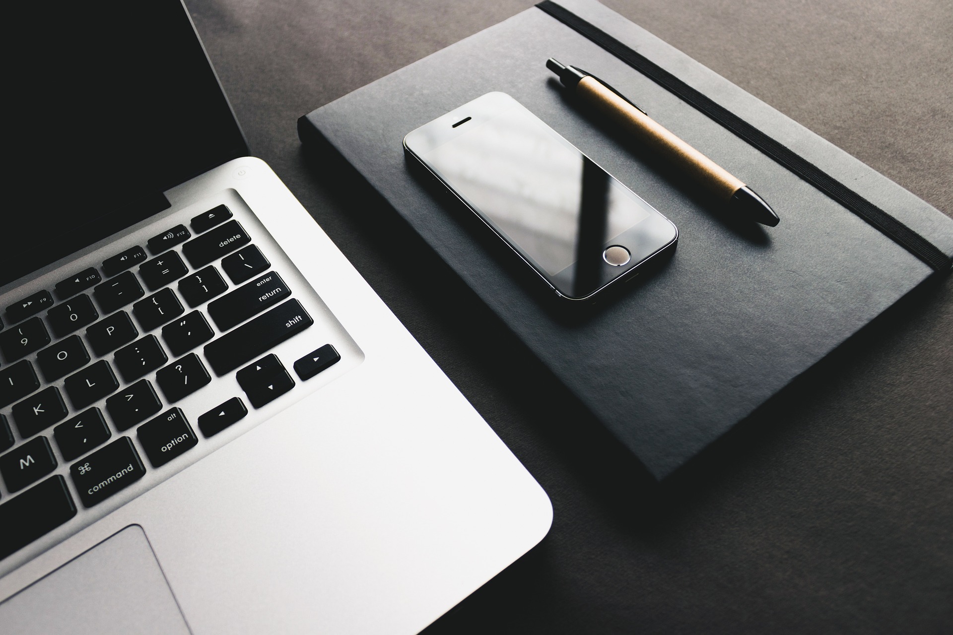 Laptop with cell phone, notebook and pen next to it.