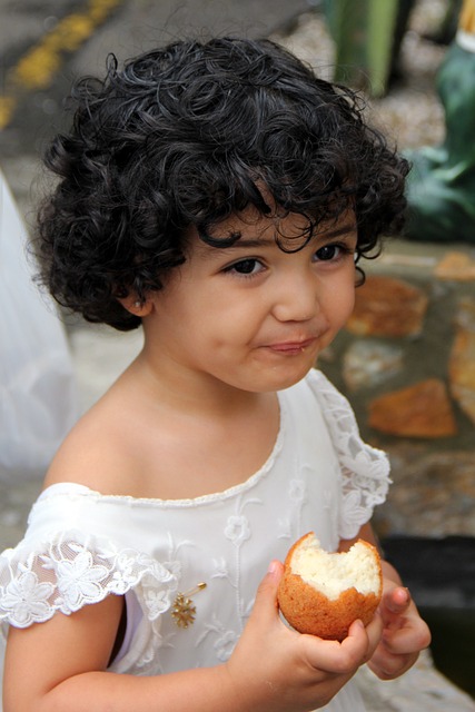 child with dark curly hair smiles while they eat an apple