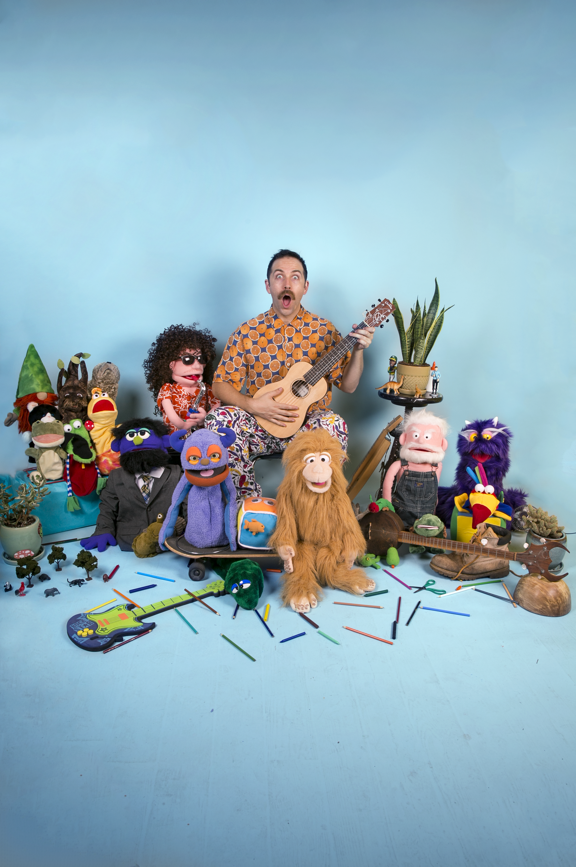 Man playing guitar with puppets around him.