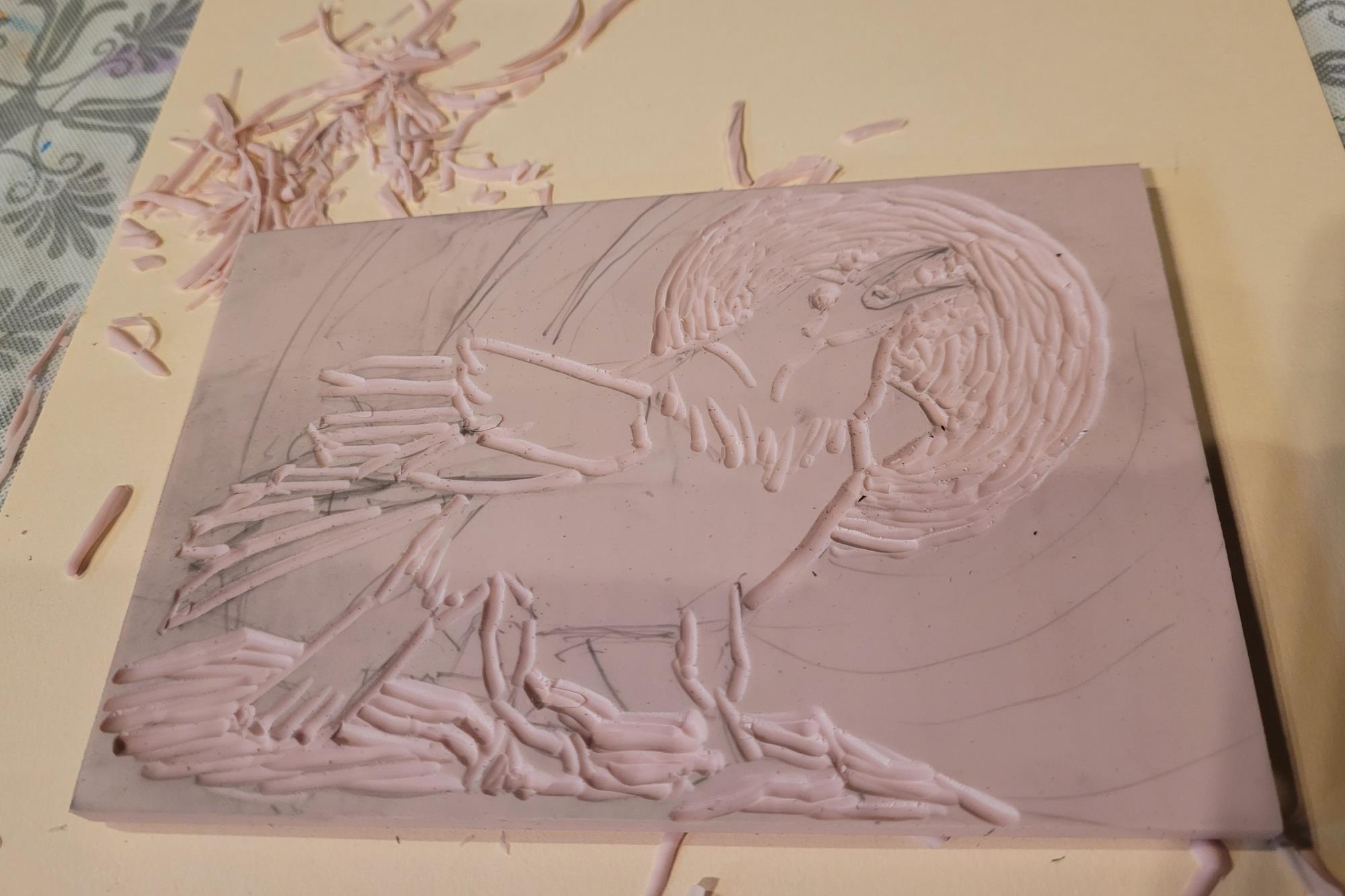 Photo of pink linoleum printing block, carved on the block is a raven with a full moon in the background. 