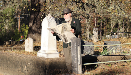 photo of man reading newspaper in a graveyard.