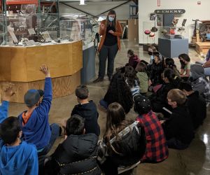 Elementary students sit on the floor and look at a museum exhibit.