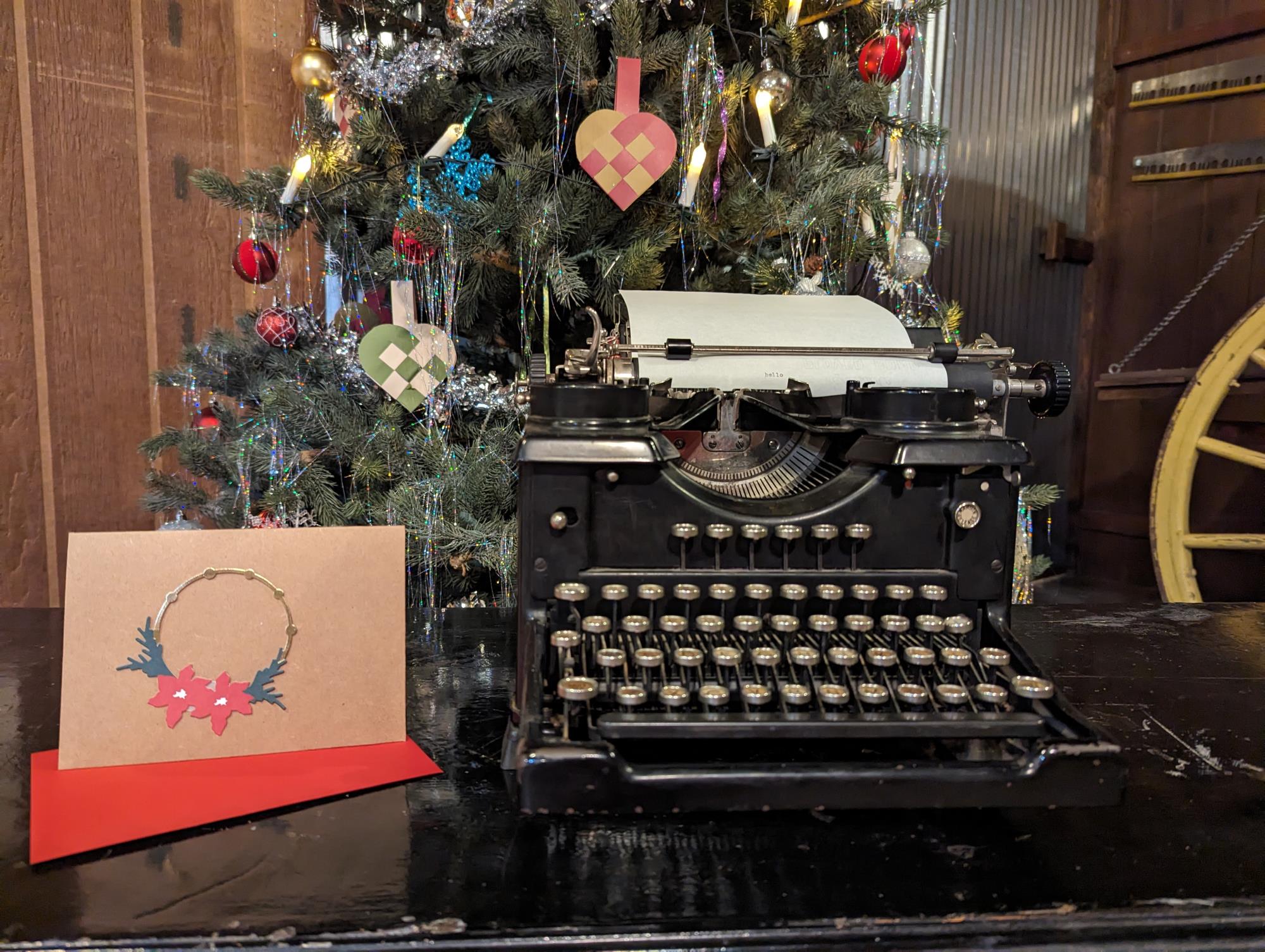 Photo of old-fashioned typewriter, a Christmas tree stands in the background. 