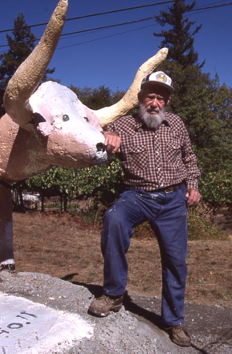 Photo of Mark Walker wearing a red and white checked shirt, next to his Oxen Sculpture