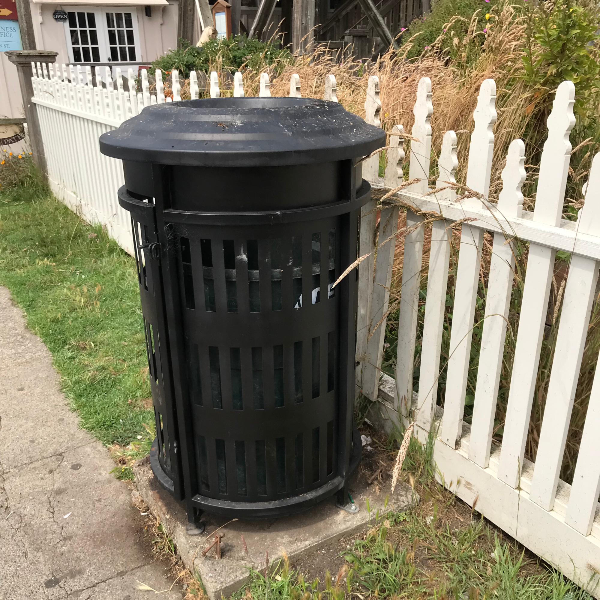 Trash can sitting next to a white picket fence