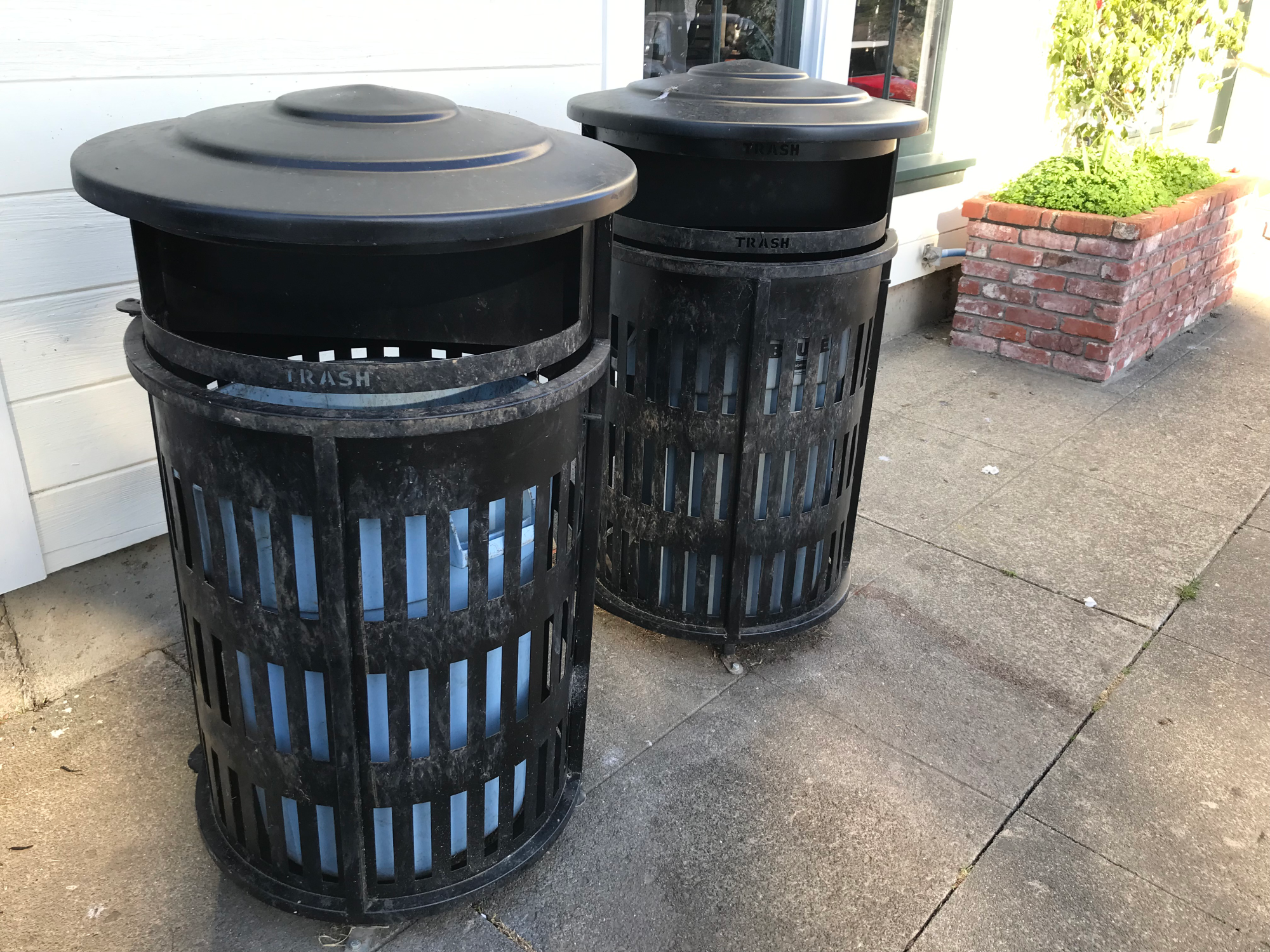 Two trash cans next to a white wall